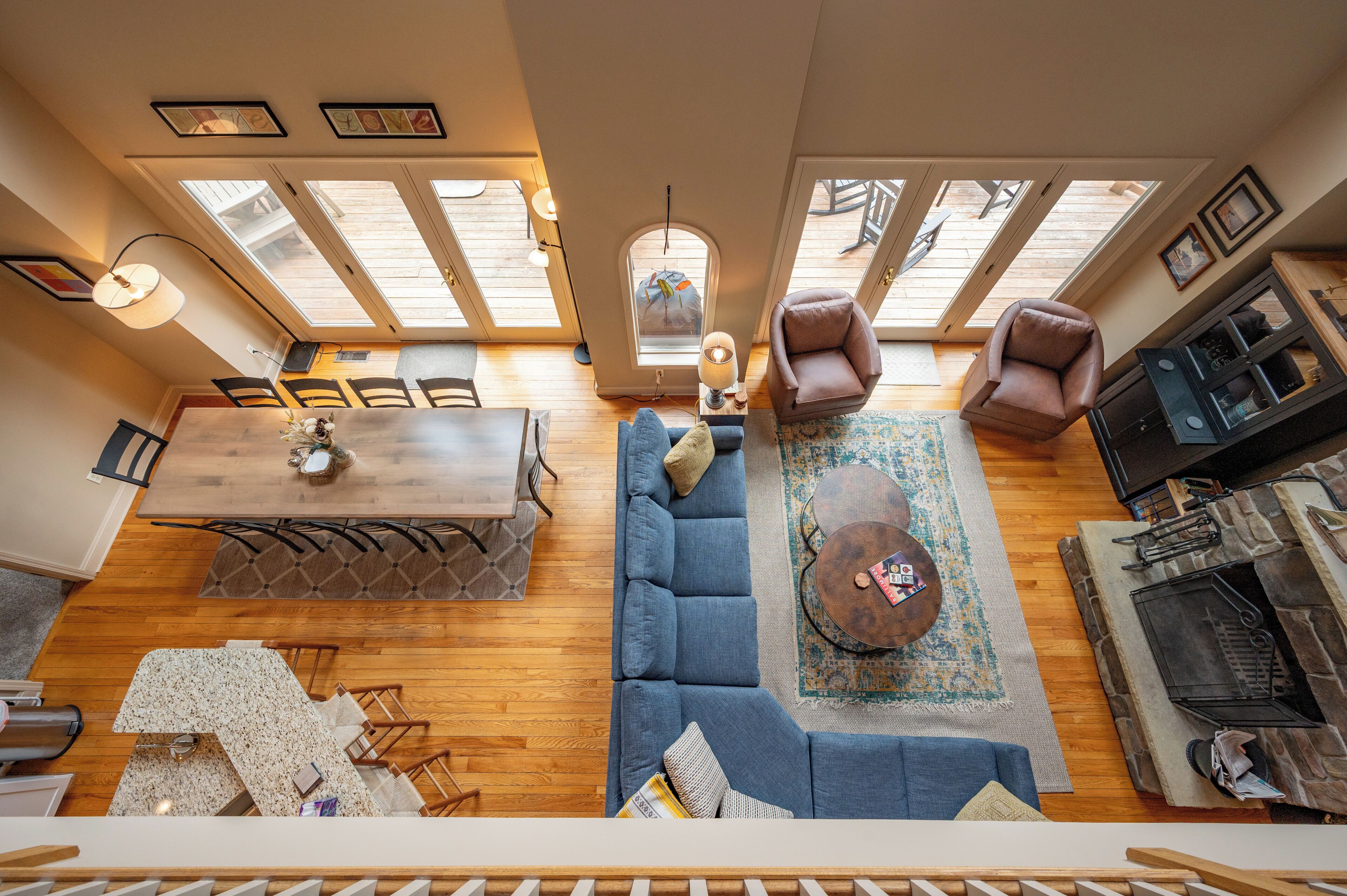 A spacious loft-style living area with a wooden floor, a blue sectional sofa, a dining table with chairs, a fireplace, and skylights.