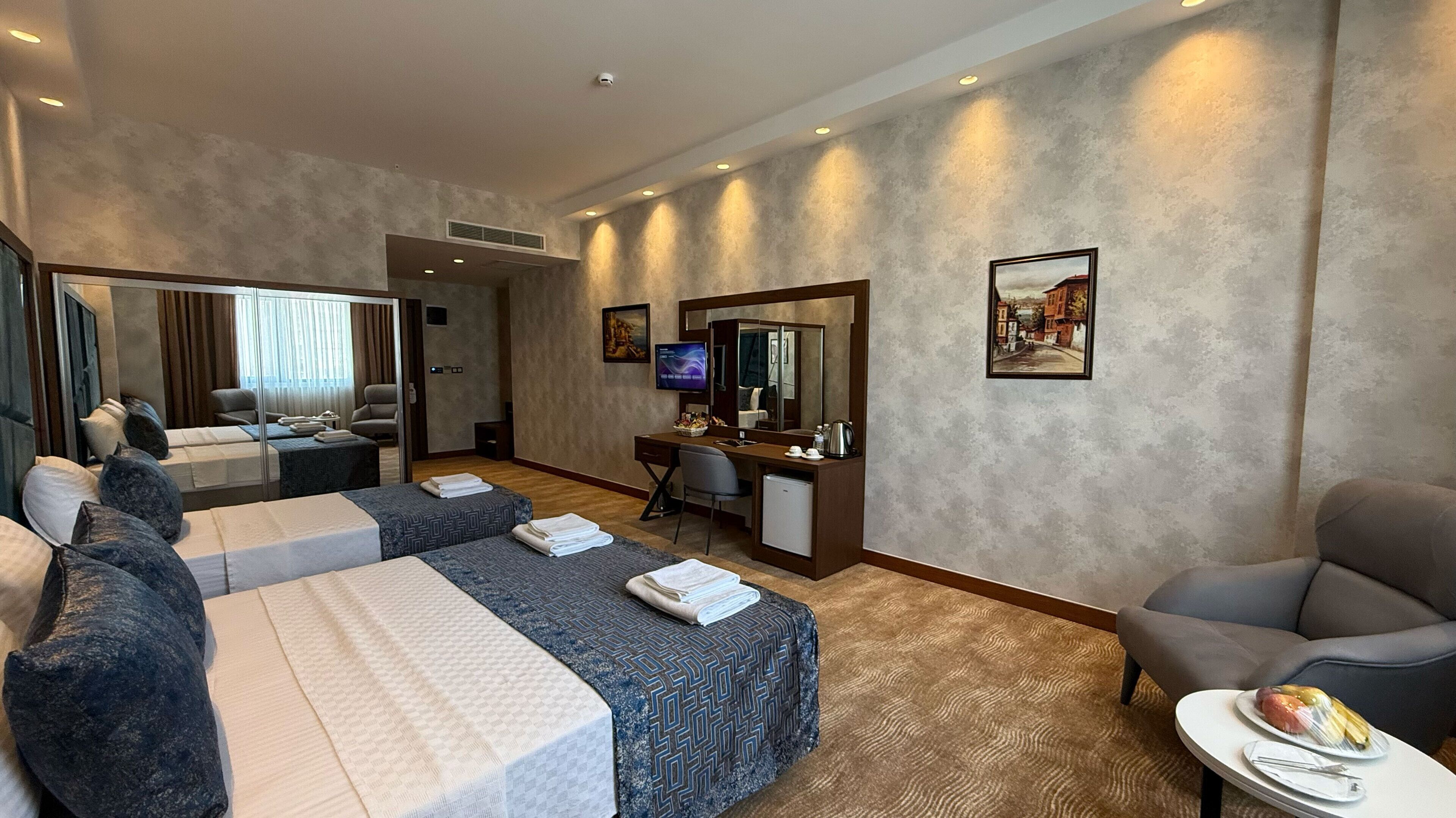 Habitación de hotel con dos camas, un escritorio, una silla, una mesita con un plato de fruta y un televisor.