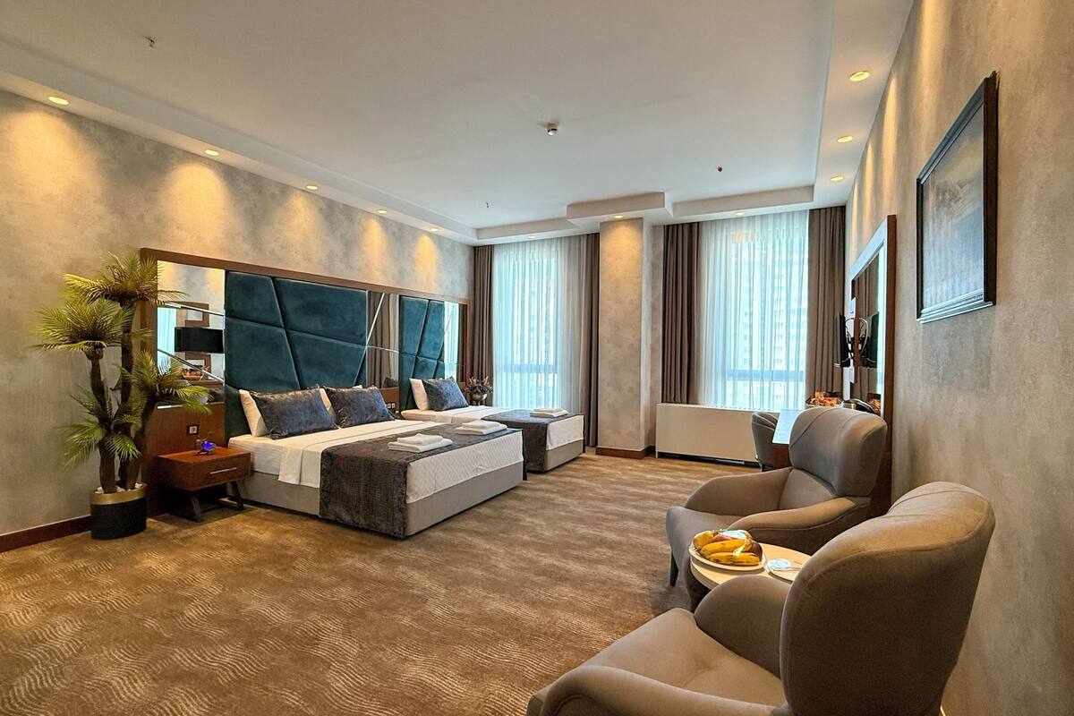 Una habitación de hotel moderna con una cama grande, un sofá, un escritorio y un ventanal amplio.