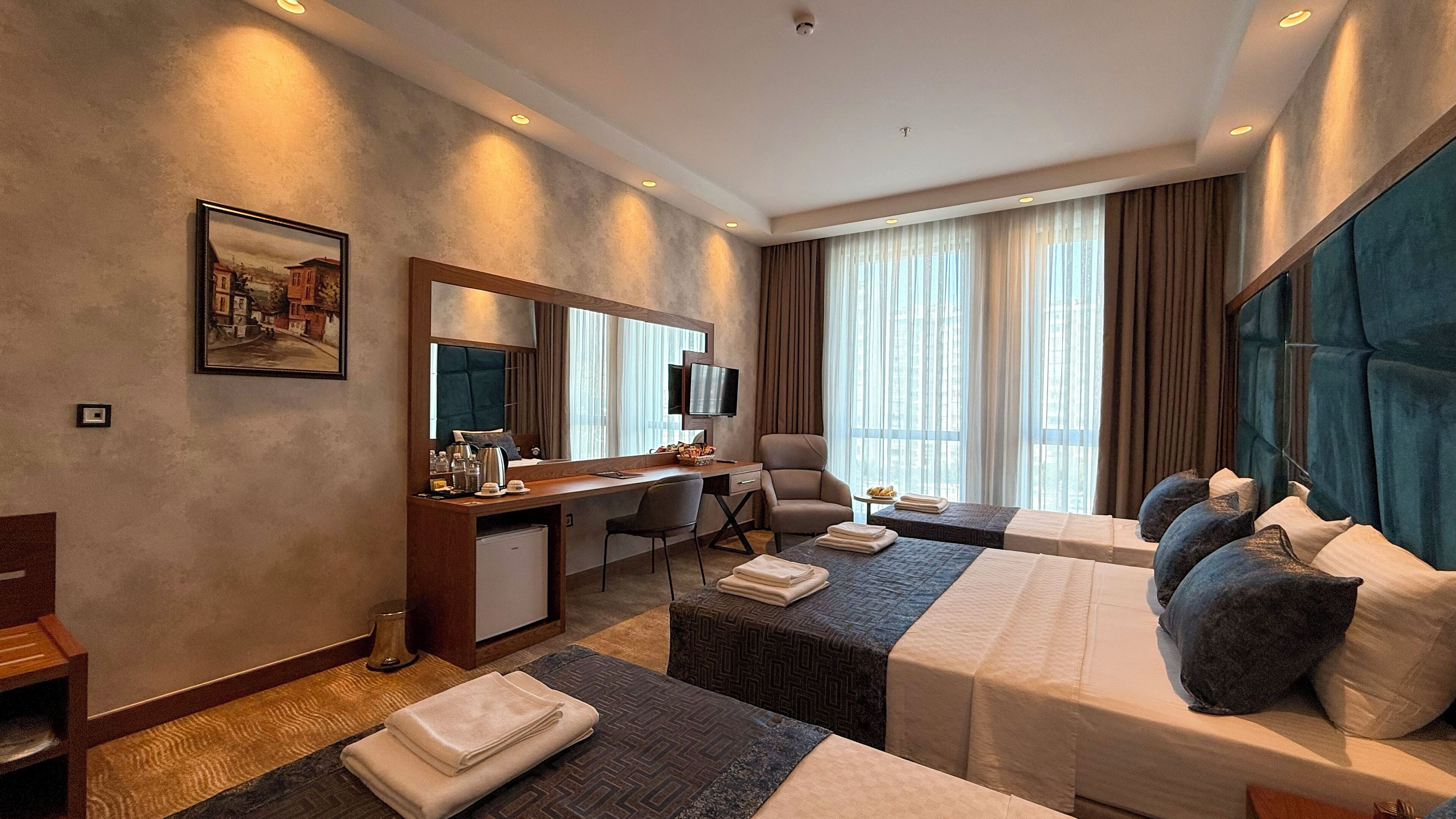 Une chambre d’hôtel avec un lit, un bureau, une chaise, une télévision et une grande fenêtre avec des rideaux.