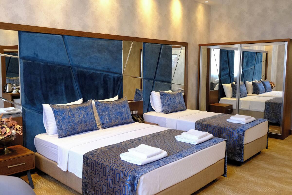 Habitación de hotel con dos camas, un espejo grande y una mesita de noche de madera con un florero.