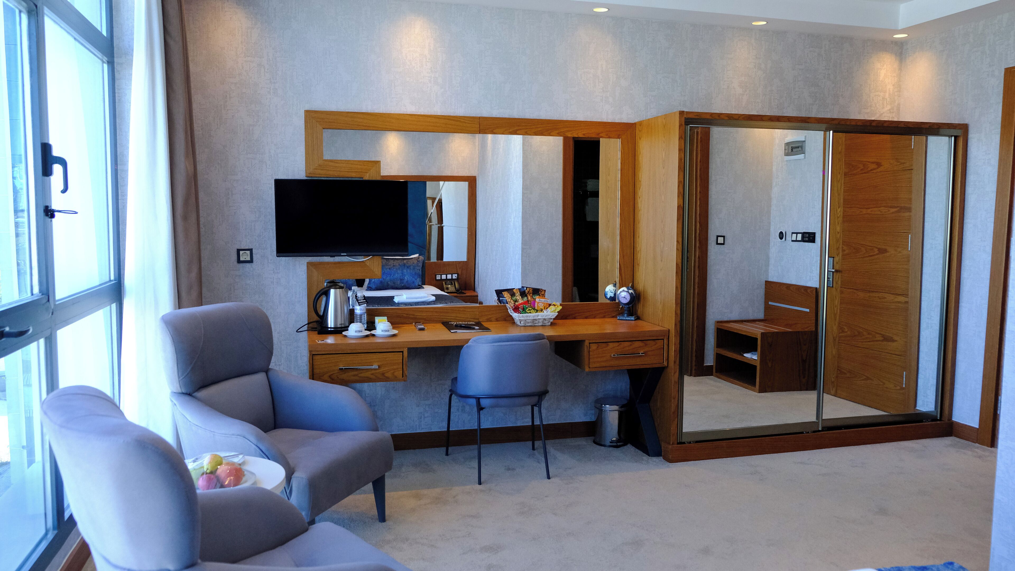 A modern hotel room with a large desk, a comfortable armchair, a television, and a mirror.