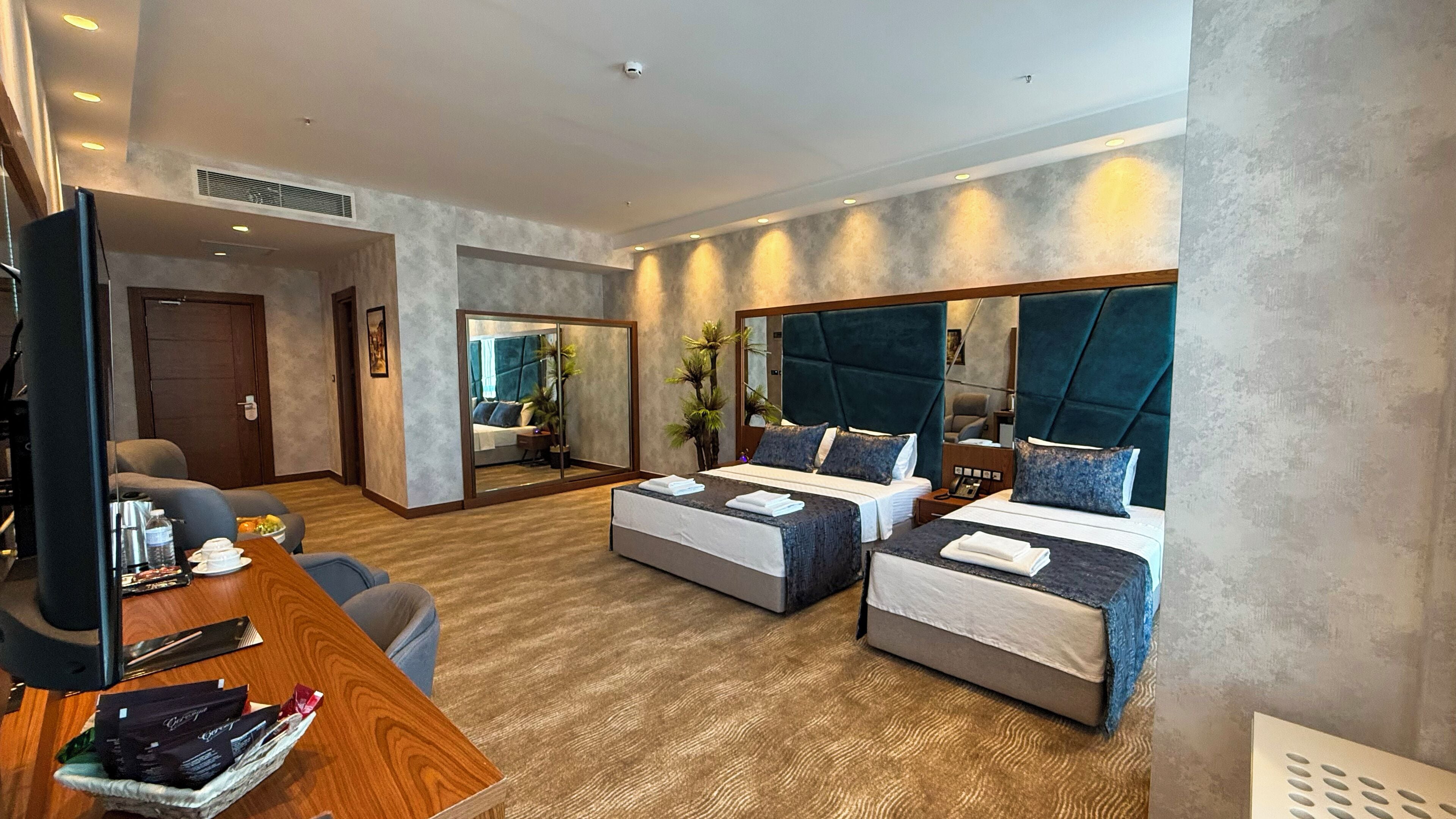 A hotel room with a large bed, a desk with a chair, a mirror, and a small seating area.