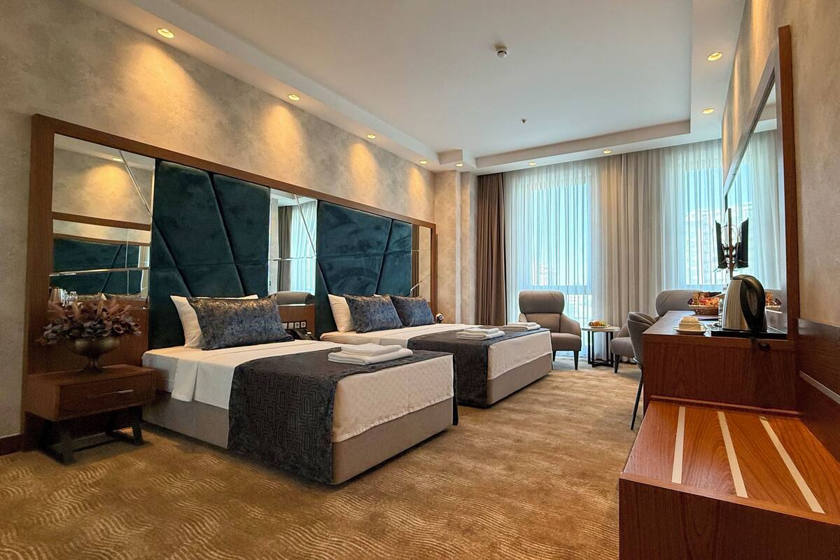 Habitación de hotel con una cama grande, un escritorio, una silla, un televisor y un espejo amplio.