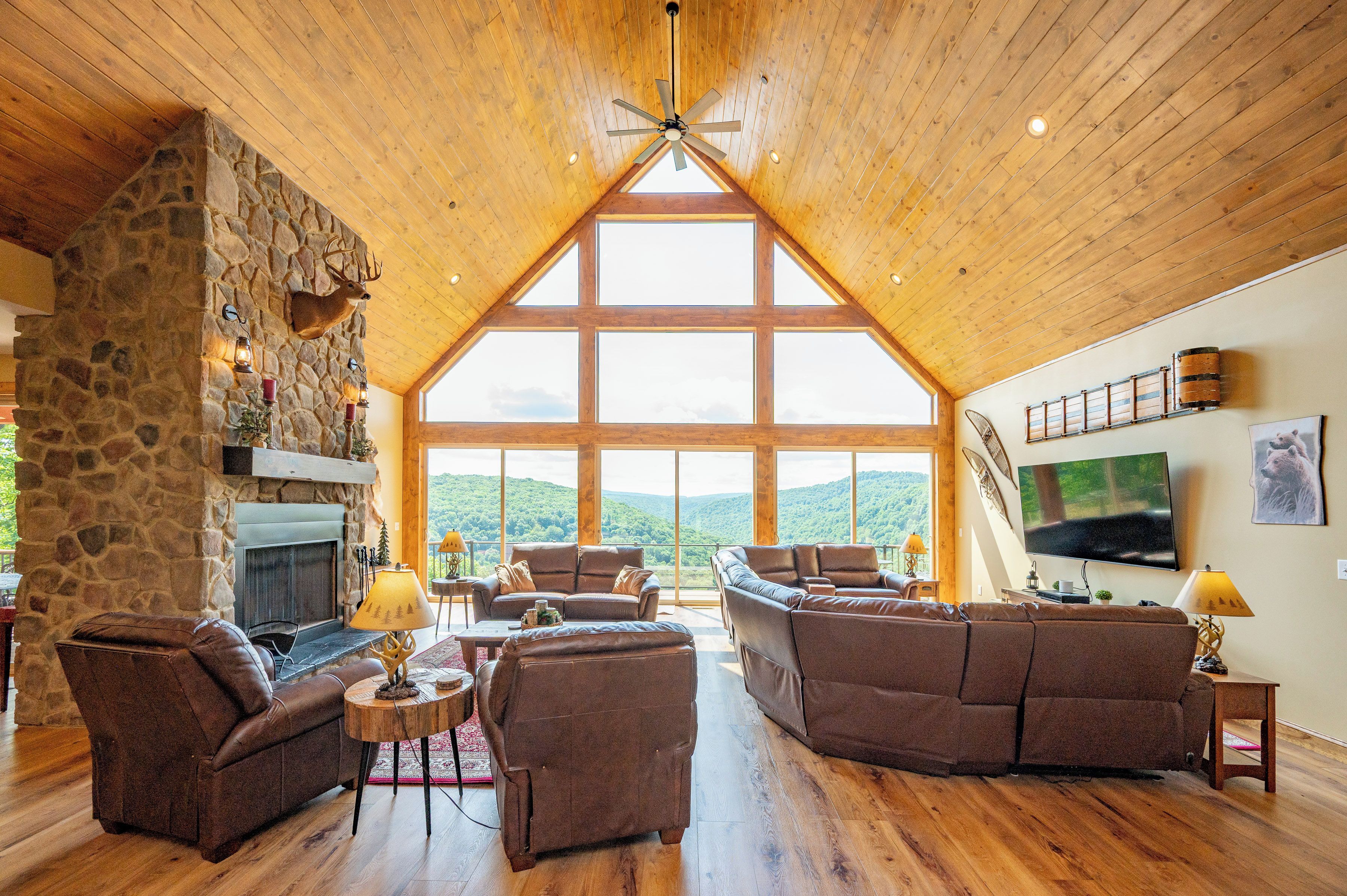 A spacious living room with a stone fireplace, leather sofas, and a large TV on the wall.