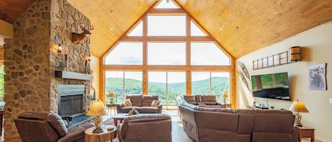 A spacious living room with a stone fireplace, leather sofas, and a large TV on the wall.