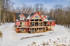 Una casa espaiosa de dos pisos amb un balcó i un porxo cobert, envoltada de neu i arbres.
