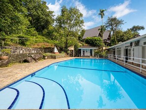 A clear blue swimming pool with a stone pathway leading to a small pavilion, surrounded by lush greenery and a stone wall. - Forest Edge Hotel (Ginigathhena)