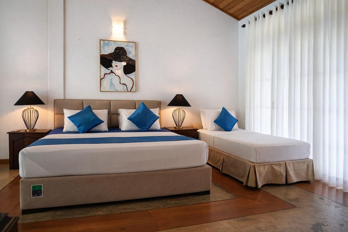 A hotel room with a large bed, two bedside tables with lamps, a painting on the wall, and a window with curtains.
