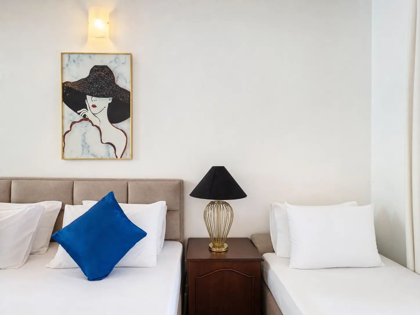 A hotel room with a bed, a nightstand with a lamp, and a wall-mounted artwork.