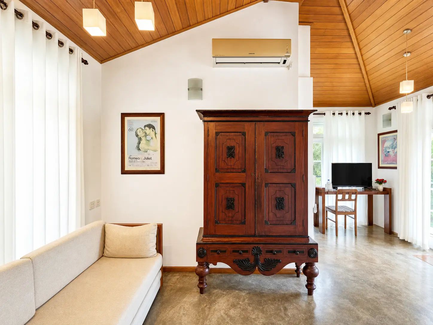 A room with a wooden ceiling, a large cabinet, a sofa, a television, and a poster on the wall.