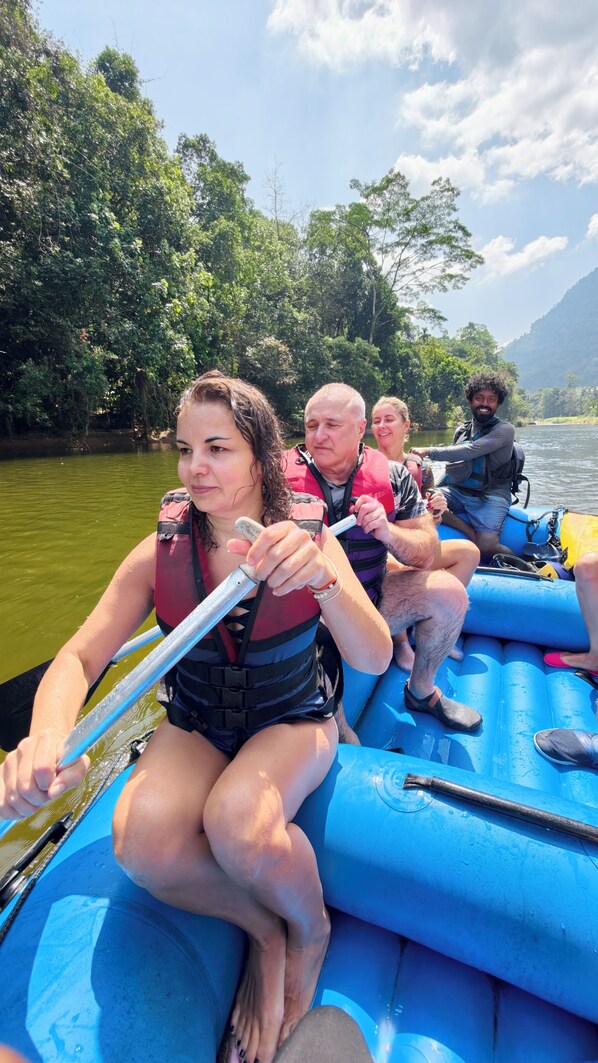 A group of people on a blue inflatable raft on a river surrounded by greenery. - Forest Edge Hotel (Ginigathhena)