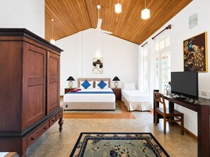 A bedroom with a wooden ceiling, a bed with blue and white bedding, a desk with a television, and a peacock painting on the wall. - Forest Edge Hotel (Ginigathhena)