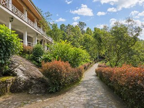 A stone pathway flanked by lush greenery and a building with a balcony. - Forest Edge Hotel (Ginigathhena)