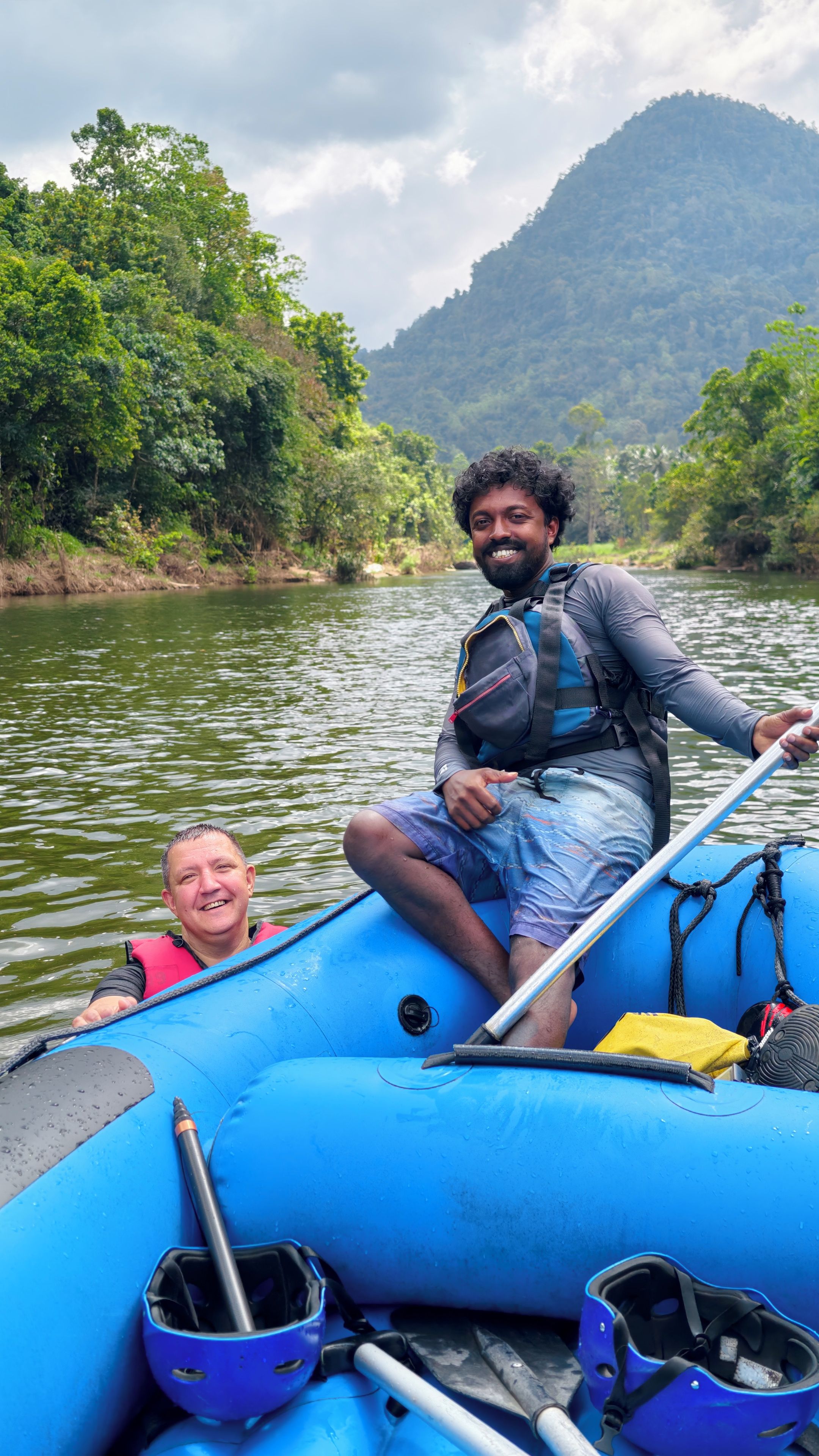 Una persona en un bote inflable azul en un río, con un paisaje boscoso al fondo.