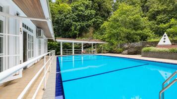 Una piscina azul cristalina con una cubierta de madera y un área de descanso techada, rodeada de abundante follaje.