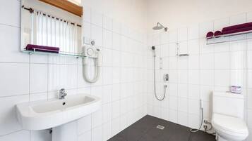 A bathroom with a white sink, a toilet, a shower, and a glass shelf with towels.