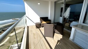 A balcony with a view of the ocean, a seating area with chairs and a table, and a glass door leading to an interior space. - 1404 Suite Frente al Mar en Cartagena (Cartagena)
