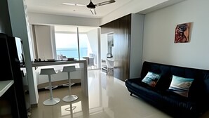 A modern living room with a black sofa, a dining area with a white table, and a view of the sea through large windows. - 1404 Suite Frente al Mar en Cartagena (Cartagena)