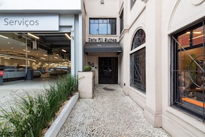 Edifício com placa 'Jate All Suites' e sinalização 'Serviços' sobre a área de recepção.