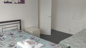 Une chambre avec deux lits, une porte blanche, un lustre et un tableau floral accroché au mur.