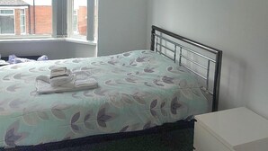 Une chambre à coucher comprenant un lit, une table de chevet, une fenêtre et une décoration florale fixée au mur.