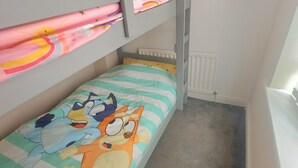 Un lit superposé avec une couette aux motifs de dessins animés et une fenêtre donnant sur le ciel.