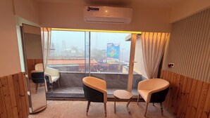 A room with two chairs and a small table, a sliding glass door leading to an outdoor area, and an air conditioning unit on the ceiling. - Ikonic Hotel - Bhushi Dam Lonavala (Lonavala)