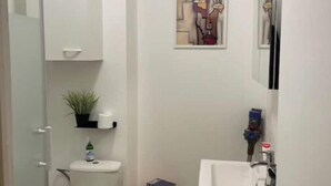 A small, modern bathroom with a toilet, sink, and shower. There is a small stool with a book and a plant on the floor. - Super apartment with free parking (Saint-Étienne)