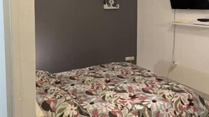A bedroom with a bed, a TV mounted on the wall, and a ceiling light. - Super apartment with free parking (Saint-Étienne)