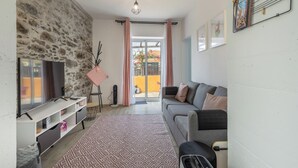 Una sala de estar con pared de piedra, un sofá, un televisor, un tapete estampado y un amplio ventanal corredizo que da a un espacio al aire libre.