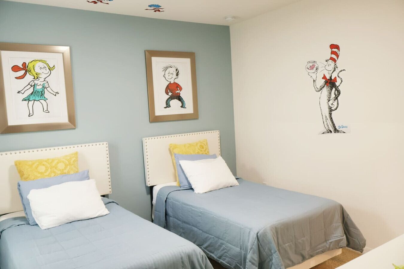 A bedroom with two beds, each with a headboard and pillows. There are framed pictures on the wall above the beds.