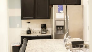 A kitchen with dark cabinets, a stainless steel refrigerator, a coffee maker, and a blender.