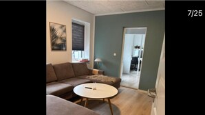 Un salón con un sofá modular, una mesa de centro redonda y una puerta que da a otra habitación.