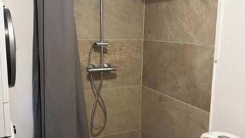 A bathroom with a shower, toilet, and a shelf with toiletries.