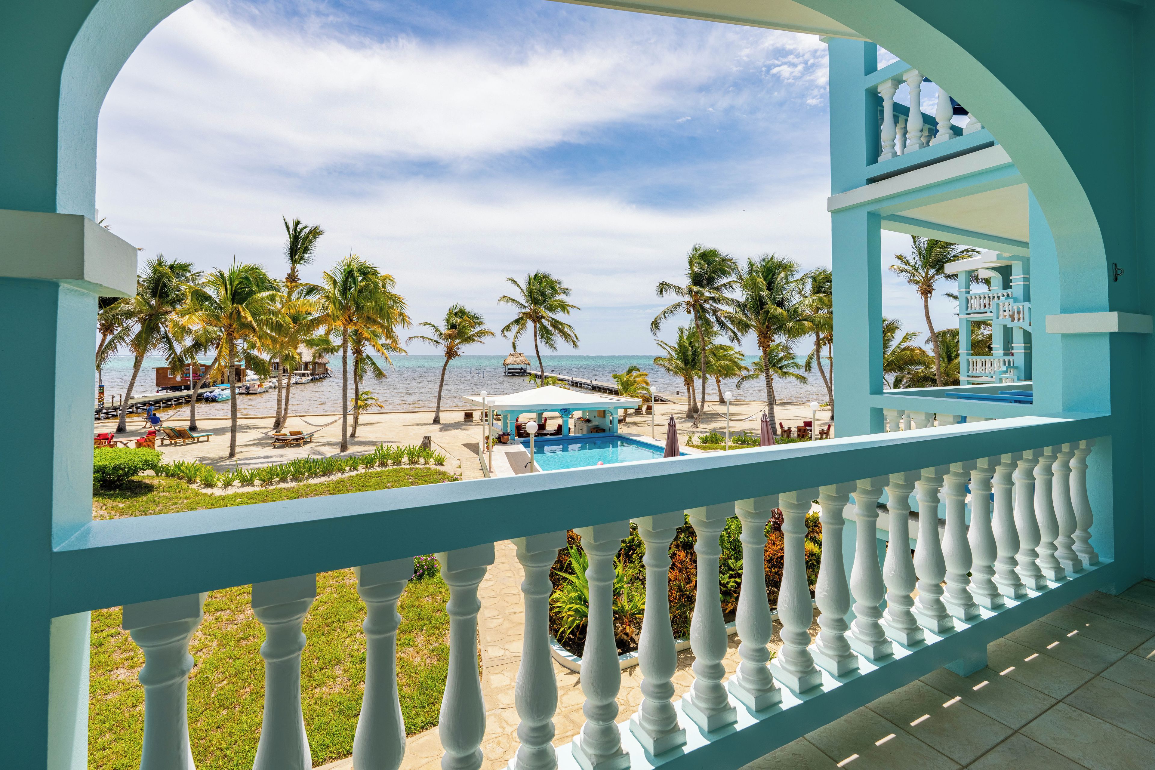 A balcony with a view of a beach, palm trees, and a pool.