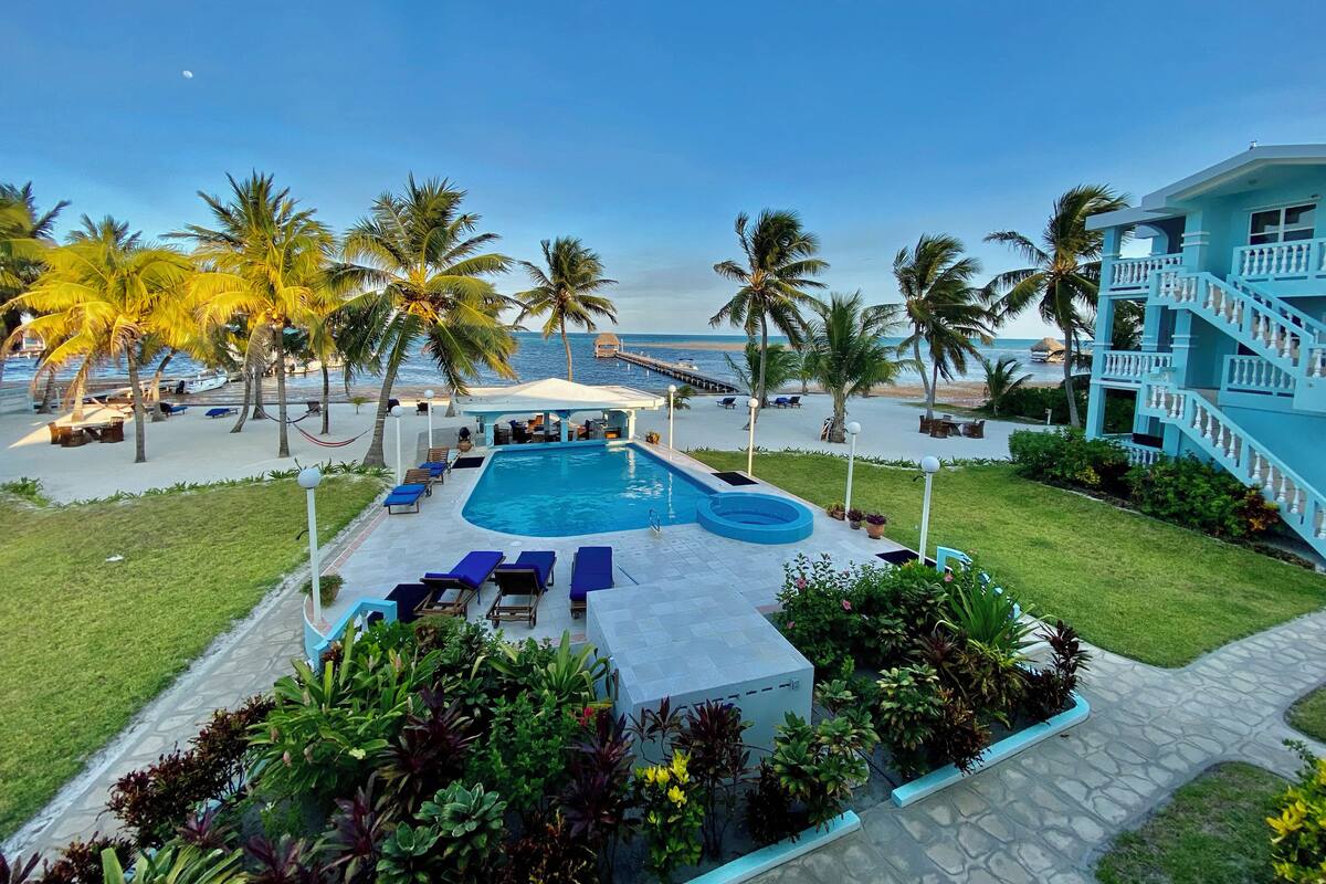 A pool area with lounge chairs, a covered seating area, and a view of the ocean.