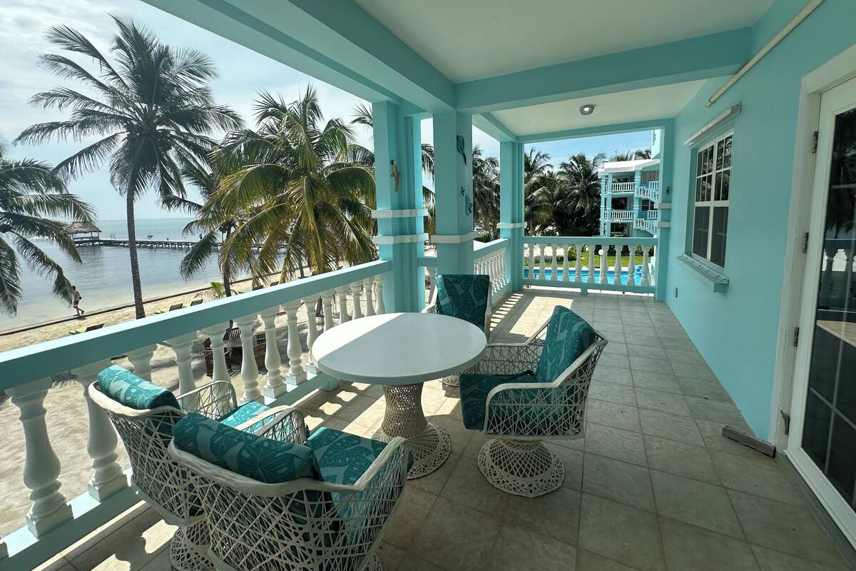 A covered balcony with a view of the beach, white wicker furniture, and a round table.