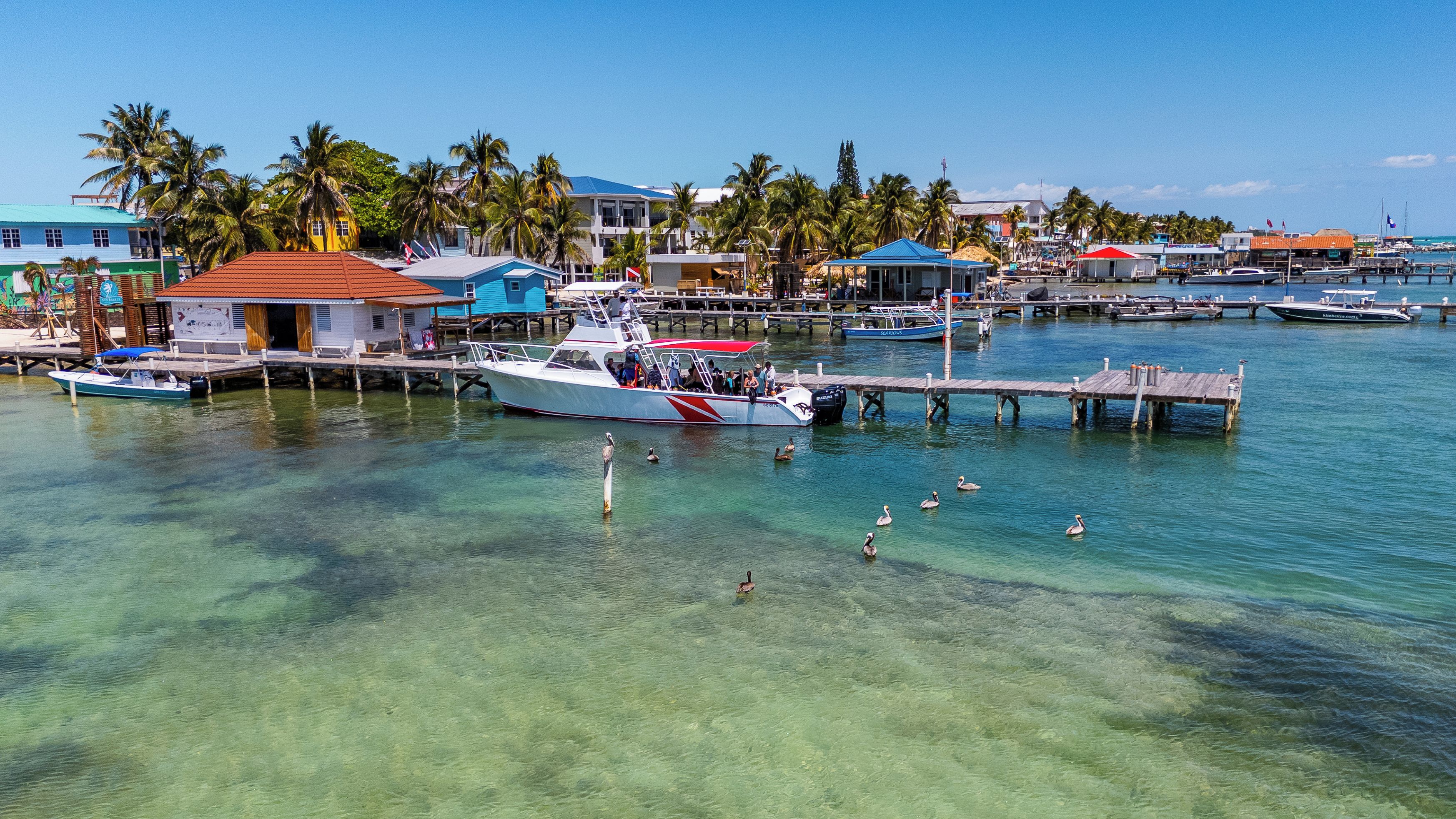 Un puerto deportivo con barcos amarrados, agua cristalina y edificios con tejados rojos.