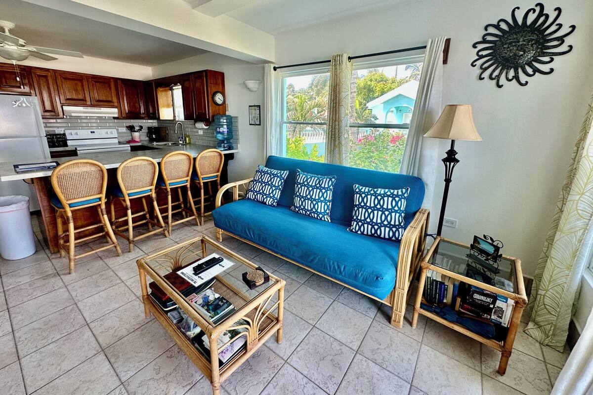 A living room with a blue sofa, wicker chairs, a glass coffee table, and a bookshelf.