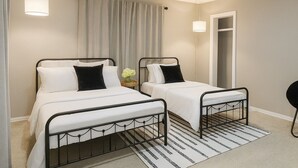 Een hotelkamer met twee eenpersoonsbedden, een kleine tafel met een bloevas, een zwarte stoel en een gestreept vloerkleed.
