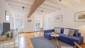 A modern living room with a blue sofa, a dining table, and a TV. - Sweett | Moscova 2b - Two Bedroom Apartment, Sleeps 5 (Milano)