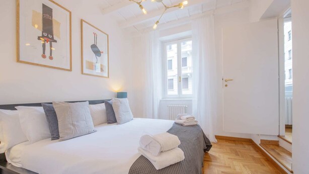 A neatly made bed with white linens and a checkered blanket, a bedside lamp, and artwork on the wall. - Sweett | Moscova 2b - Two Bedroom Apartment, Sleeps 5 (Milano)