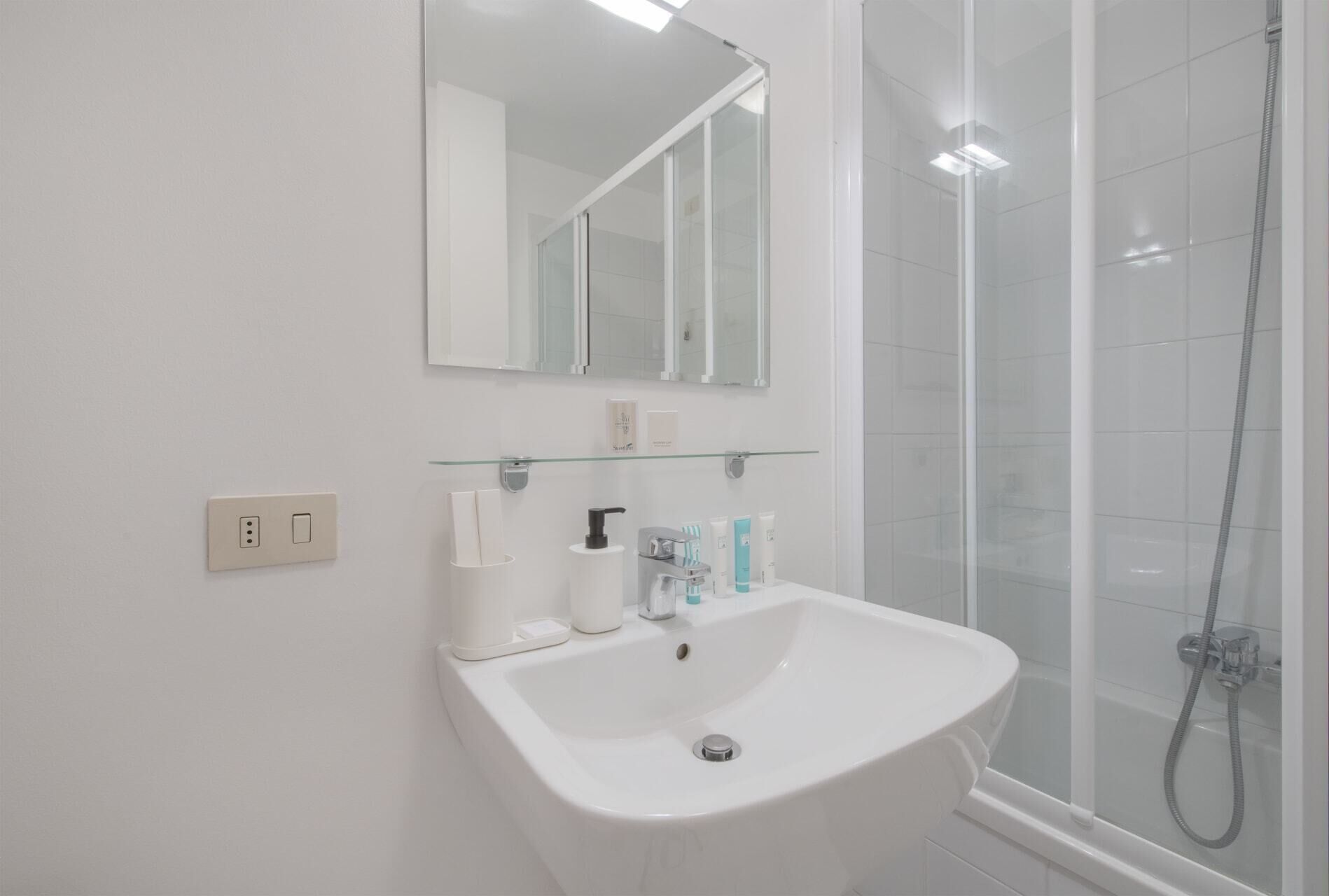 Un baño moderno con un lavabo blanco, cabina de ducha de vidrio y un espejo sobre el lavabo.