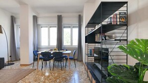 A dining area with a table and chairs, a bookshelf, and a large plant. - Sweett | Fontana - Two Bedroom Apartment, Sleeps 5 (Milano)