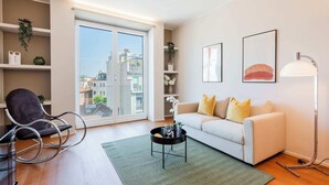 A modern living room with a sofa, a coffee table, a rocking chair, and a floor lamp. There is a large window with a view of buildings outside. - Sweett | Luxury Velasca IV (Milano)