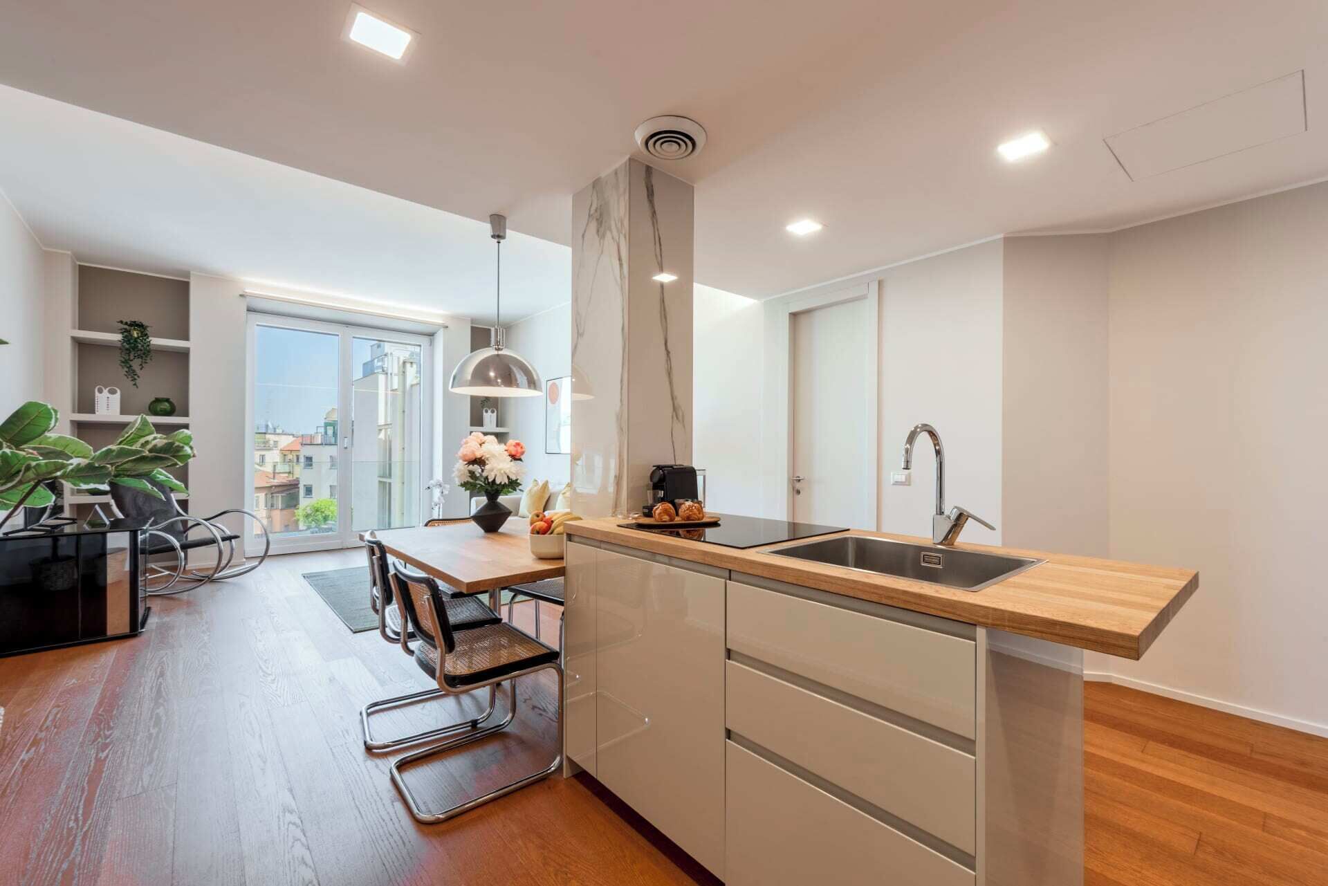 Una cocina moderna con encimera de madera, lavaplatos de acero inoxidable y comedor con mesa y sillas.