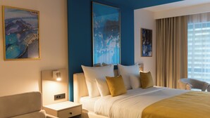 A hotel room with a large bed, a bedside table, a chair, and artwork on the walls.