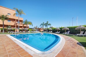 Una piscina con sillas de descanso, palmeras y un edificio al fondo.