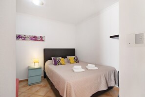 Un dormitorio con cama, mesita de noche, lámpara y una obra de arte en la pared.